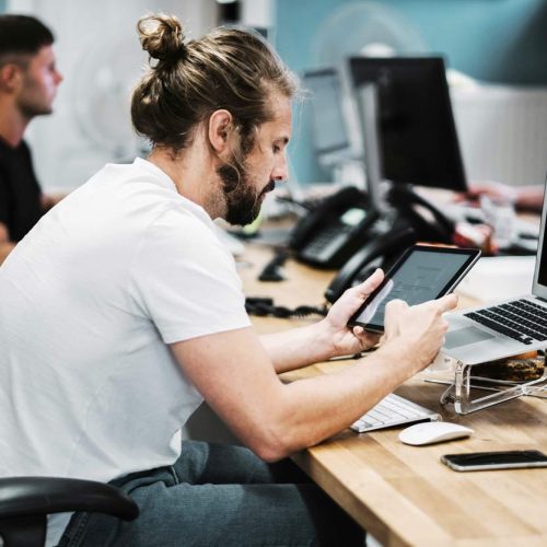 A man sitting at a desk, focused on his tablet computer, working diligently, testing application.