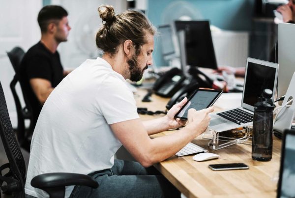 A man sitting at a desk, focused on his tablet computer, working diligently, testing application.