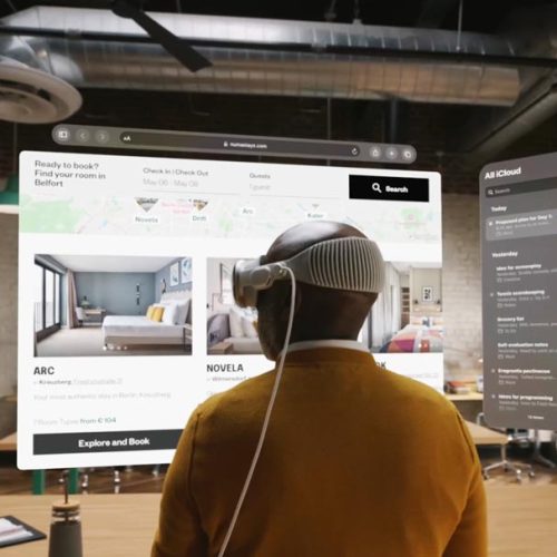 A person wearing a virtual reality headset interacts with multiple floating, computer-generated screens in a modern, industrial-style office space.