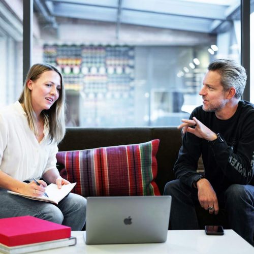 A man and woman sitting on a couch with a laptop, working together at modern office testing an application.