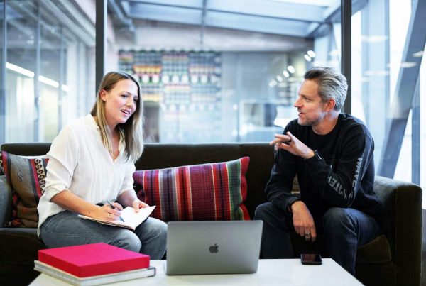 A man and woman sitting on a couch with a laptop, working together at modern office testing an application.