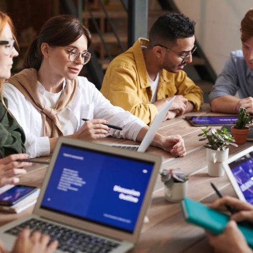 A diverse group of individuals sitting around a table, engrossed in their work on laptops.