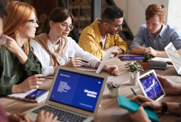 A diverse group of individuals sitting around a table, engrossed in their work on laptops.